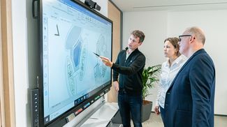Drei Mitarbeitende diskutieren eine Planung am Touchscreen-Whiteboard