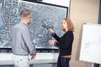 Zwei Mitarbeitende betrachten eine Luftbildaufnahme einer Innenstadt auf einem Whiteboard